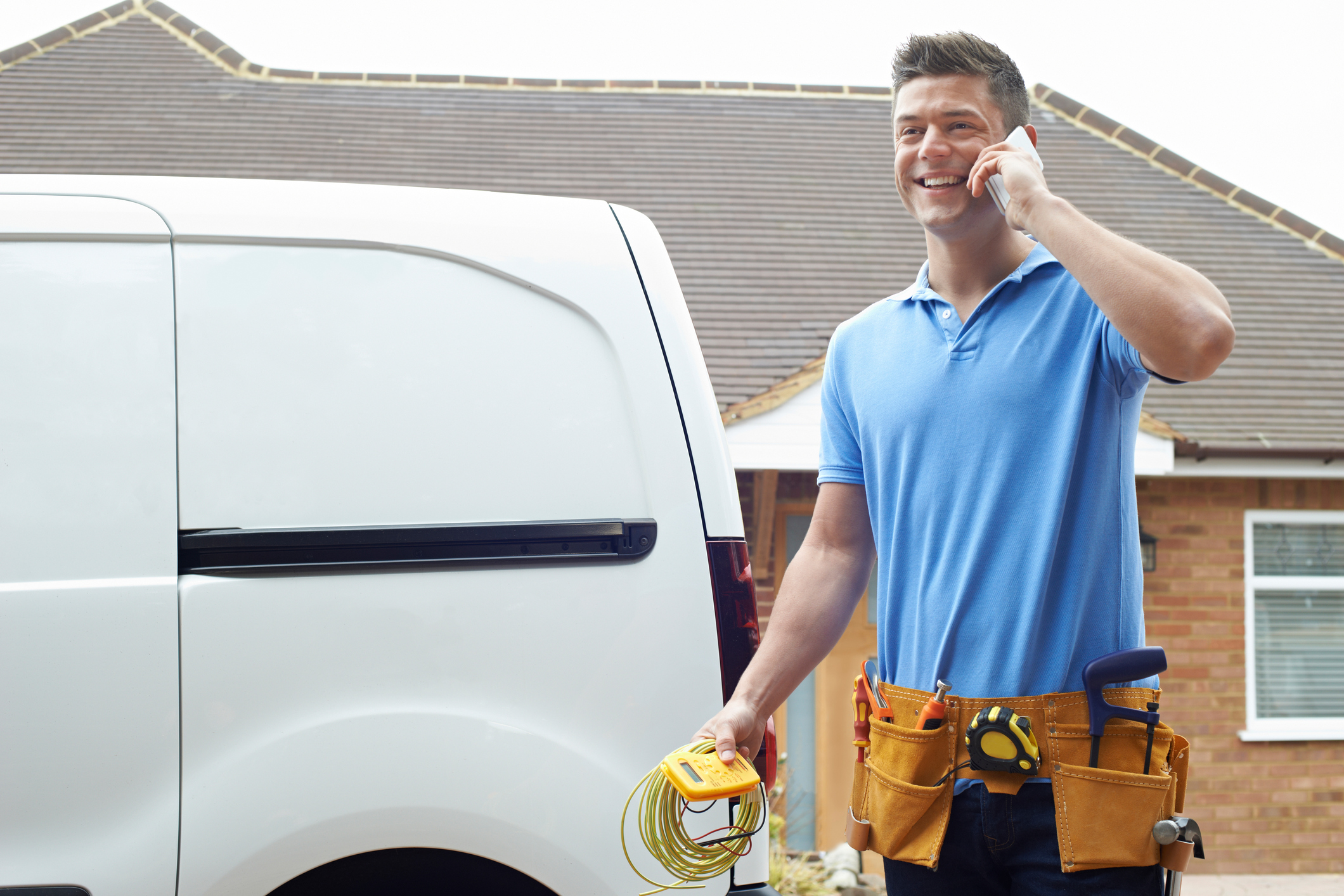 HVAC technician on the phone in front of a white work van in a residential neighborhood