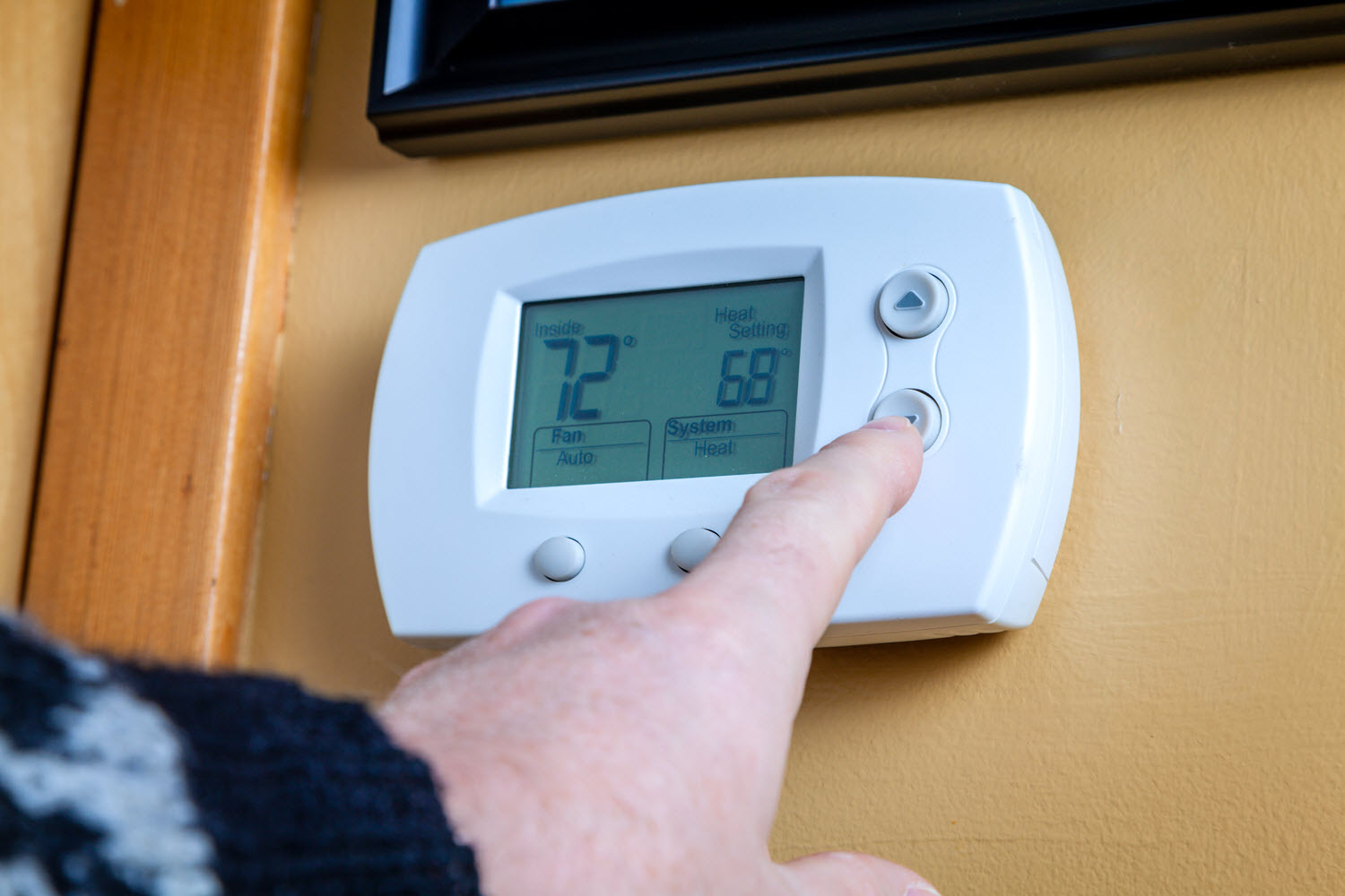 Hand of a homeowner on a wall-mounted thermostat