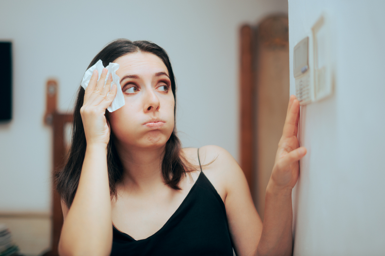 Woman wiping sweat off her head while looking at her thermostat