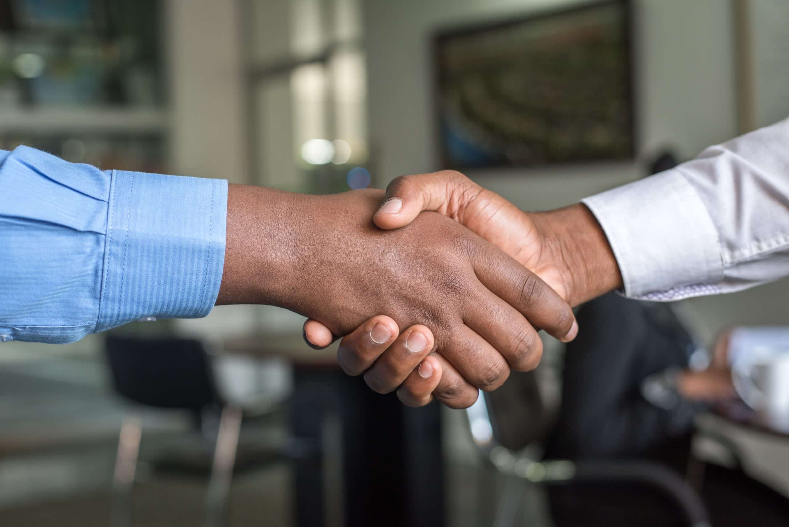 Two people shaking hands, one in a blue shirt & one in a white shirt