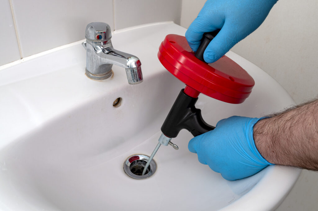 plumber repairing drain with plumbers snake (steel spiral that twists through pipes to collect dirt) in residential sink